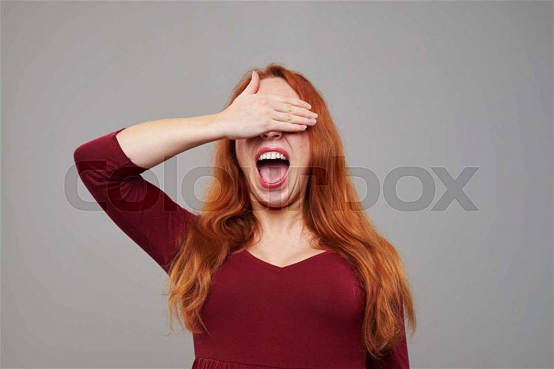 Close-up portrait of surprised young woman with red hair waiting for something with closed eyes. Isolated over background , stock photo
