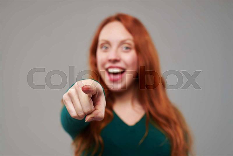 Rack focus on an index finger given by redhead young woman in the studio. Female isolated over gray background , stock photo