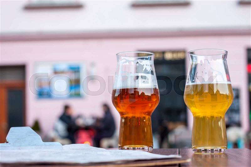 Two glasses of beer on table edge outside bar background, stock photo