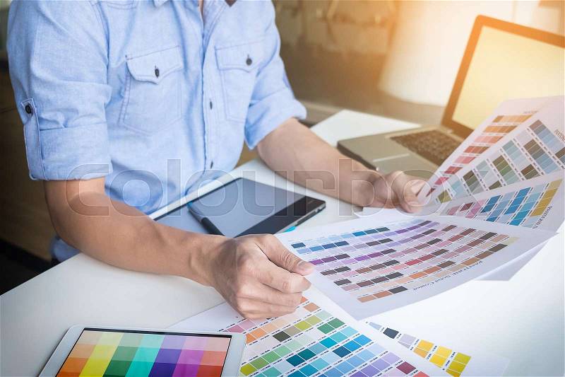 Young graphic designer working on a desktop computer and using some color swatches, stock photo