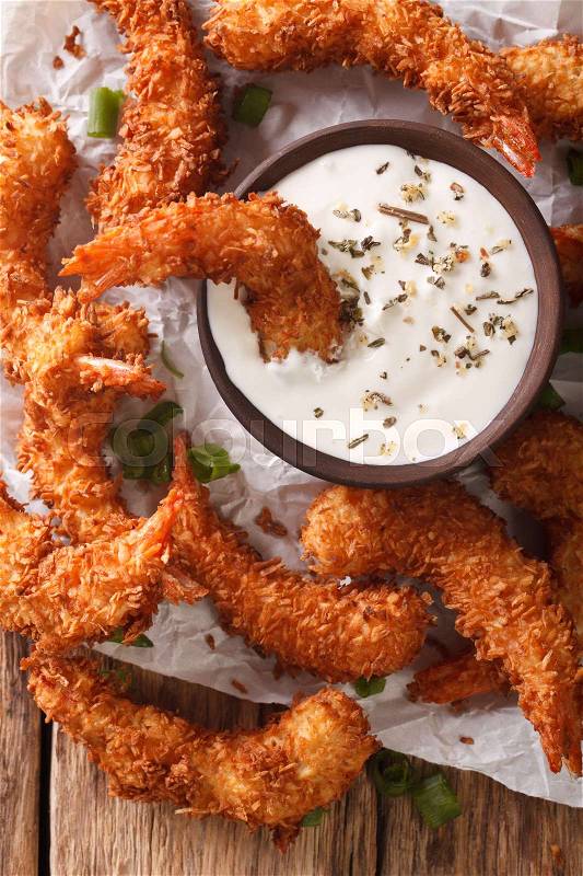 Fried coconut shrimp close-up and a cream sauce on the parchment on the table. vertical view from above , stock photo