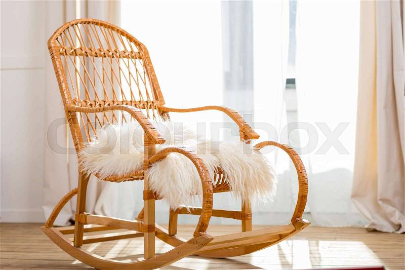 Rocking chair with woolly rug in bright room with sunlight, stock photo