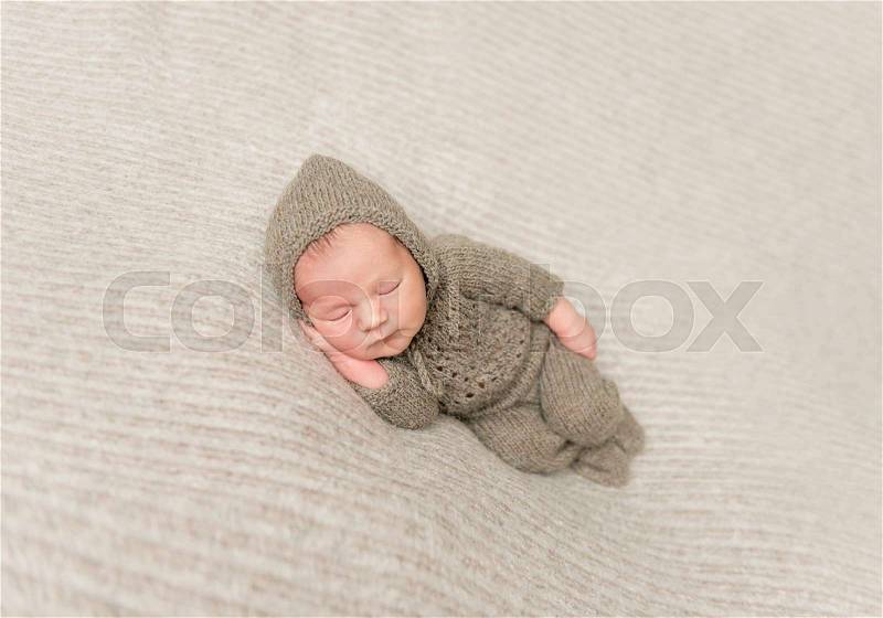 Sweet infant taking a nap in brown knitted clothes, on side, hand under his cheek, stock photo