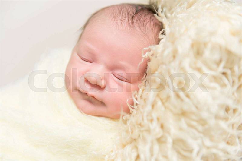 Sweet hairy baby sleeping on a furry yellow pillow, wrapped up with a blanket, closeup, stock photo