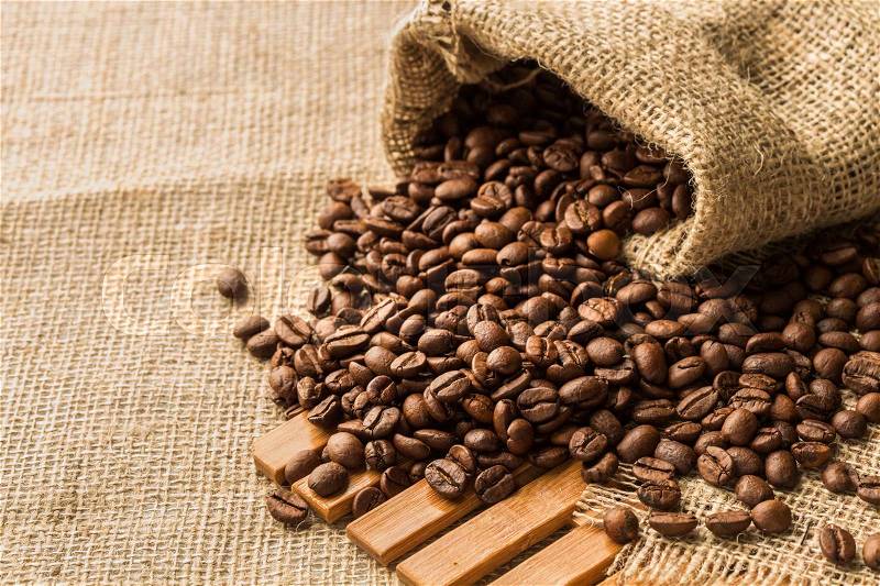 Coffee beans in a burlap bag on a wooden background, stock photo