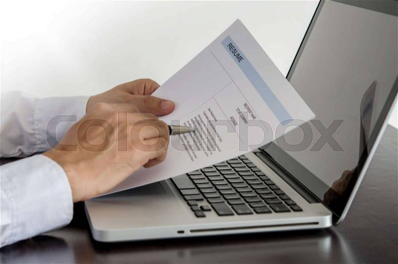Businessman or job seeker review his resume on his desk with pen and computer laptop, stock photo