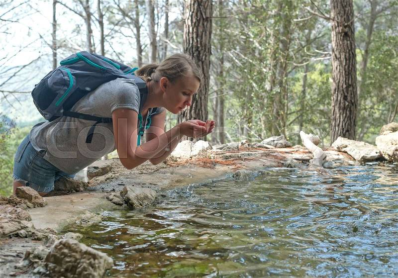 Woman with backpack drinking water from mountain spring, stock photo