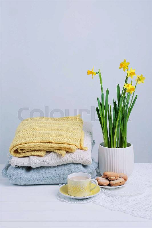 Indoor table setting. Narcissus flower in a pot with a pile of knitted sweaters cookies and tea cup, stock photo