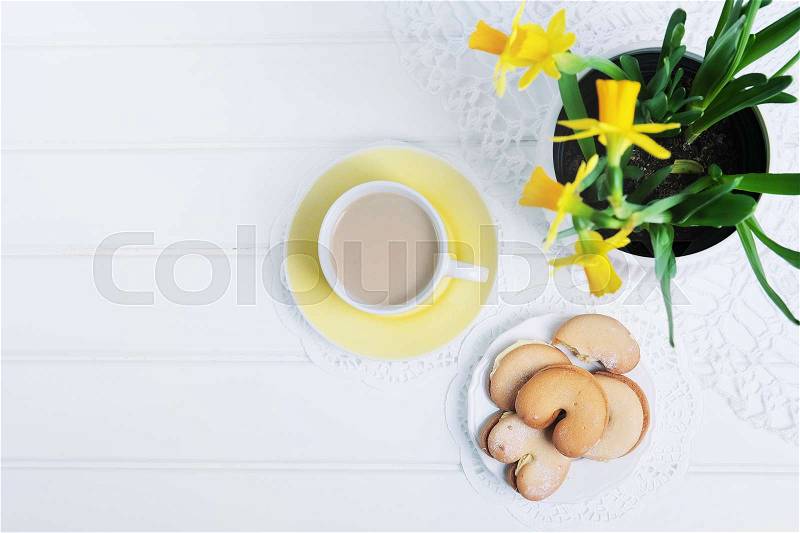 Indoor table setting. Narcissus flower in a pot with cookies and tea cup, stock photo