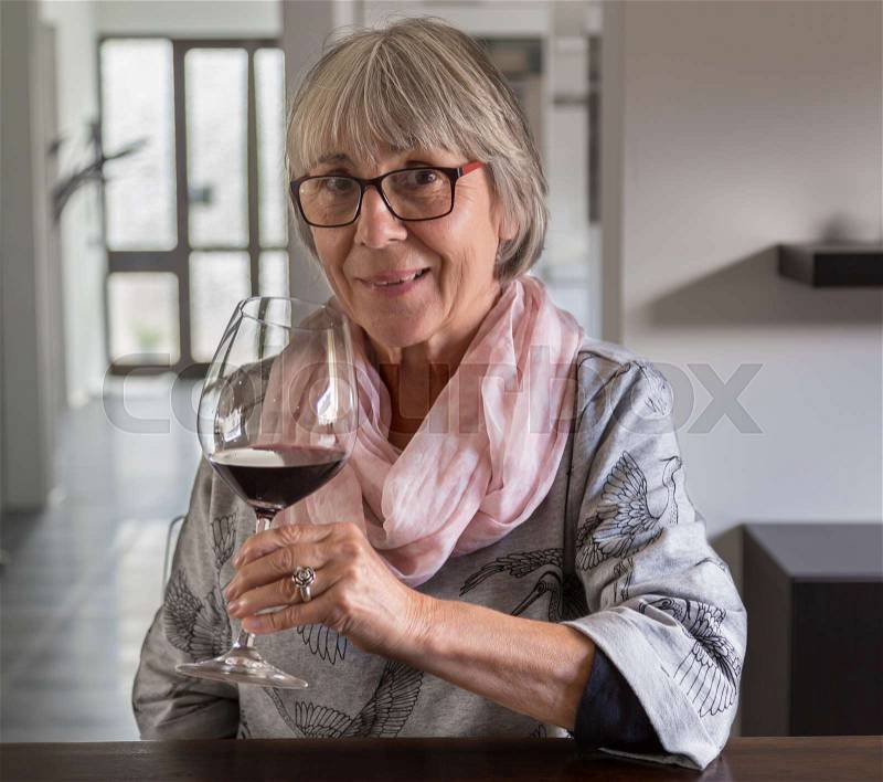Senior woman drinking wine at a table, stock photo
