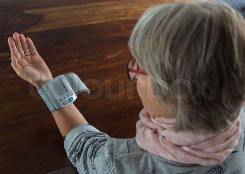 Senior checks blood pressure with measuring instrument on table, stock photo