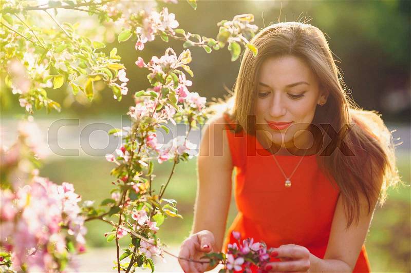 Beautiful young woman smelling a flower in the spring park, stock photo