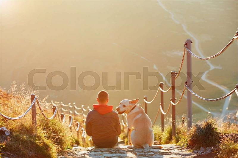 Man with dog on the trip in the mountains. Young tourist and his dog are resting and together watching the sunset. - , stock photo