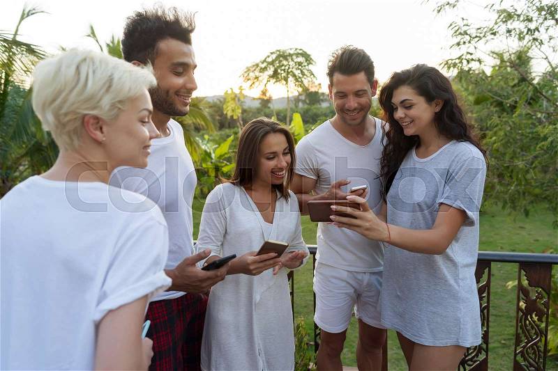 Young People Group On Terrace Tropical Hotel, Friends Using Cell Smart Phone Tropic Holiday Vacation Green Forest, stock photo