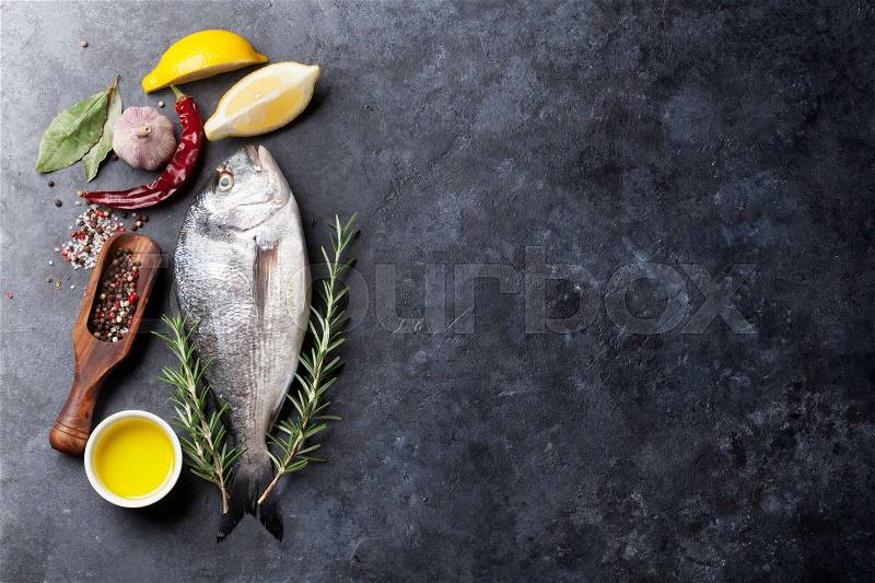 Raw fish cooking and ingredients. Dorado, lemon, herbs and spices. Top view with copy space on stone table, stock photo