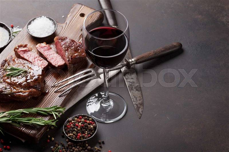 Grilled ribeye beef steak with red wine, herbs and spices on stone table, stock photo
