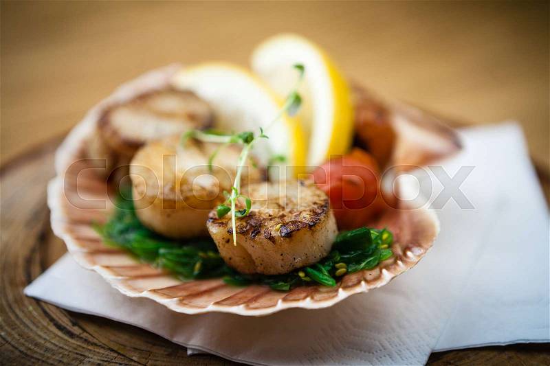 Fried scallops with lemon, cherry tomatoes served on a shell, stock photo