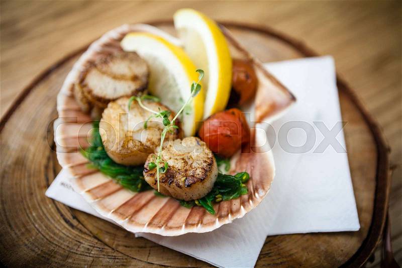 Fried scallops with lemon, cherry tomatoes served on a shell, stock photo