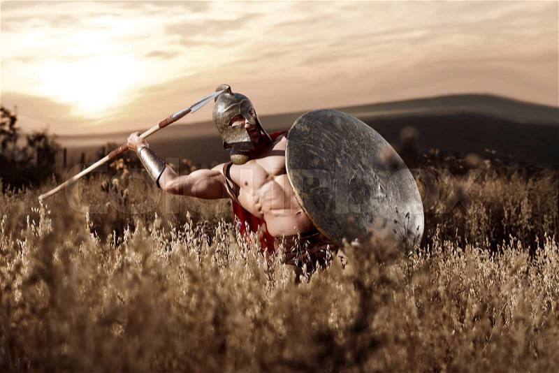 War god. Sepia toned shot of a muscular strong Roman legionary warrior with perfectly shaped athletic body throwing his spear during the battle in the field on dusk power fearless war concept, stock photo