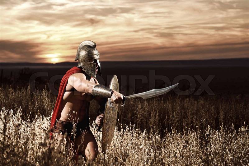 Sepia toned portrait of a muscular Spartan soldier wearing a helmet and a cape guarding against his enemy with a shield holding a sword in his hand copyspace, stock photo