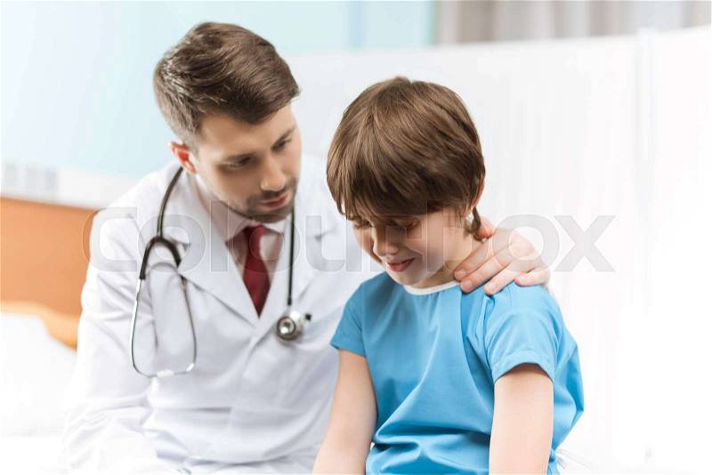 Portrait of doctor cheering up little crying boy in hospital, stock photo
