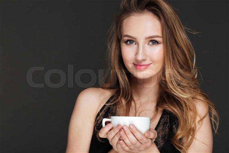 Picture of young amazing woman holding cup of coffee over dark background dressed in lingerie, stock photo