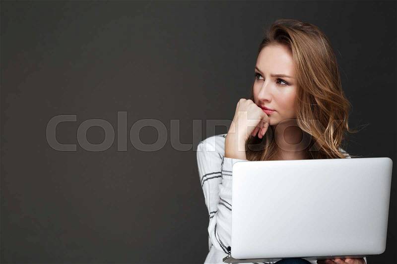 Image of young serious lady using laptop over dark background dressed in shirt, stock photo