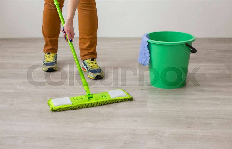 Woman mopping the floor in a living room with a colorful green mop, stock photo