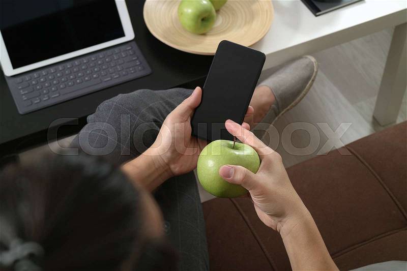 Hipster hand using smart phone for mobile payments online business,omni channel,sitting on sofa in living room,green apples in wooden tray, stock photo