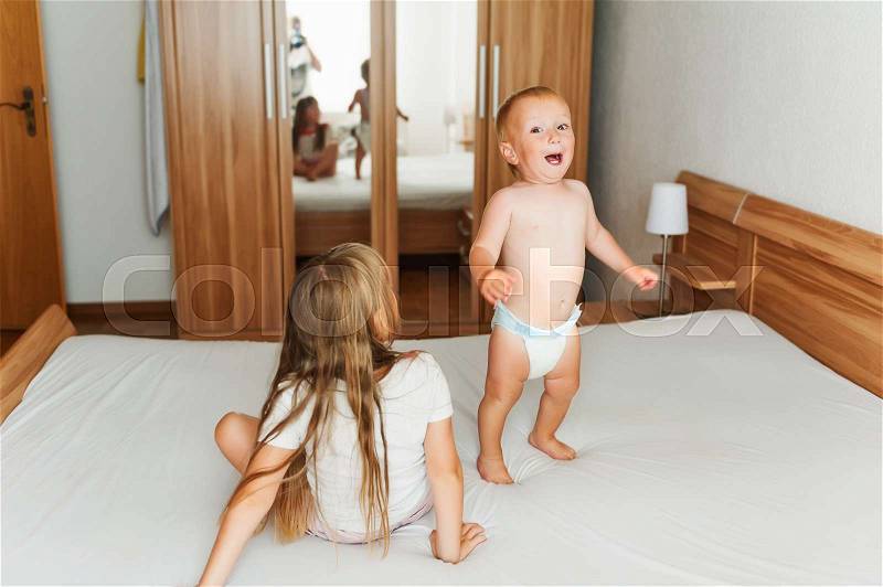 Mother taking pictures of two happy kids jumping on the bed, stock photo