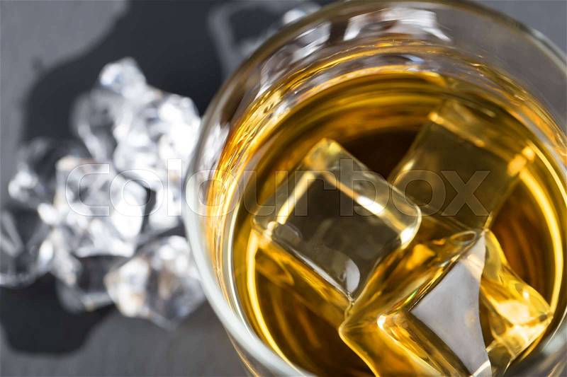 A fragment of a round glass of whiskey with ice on a dark background, stock photo