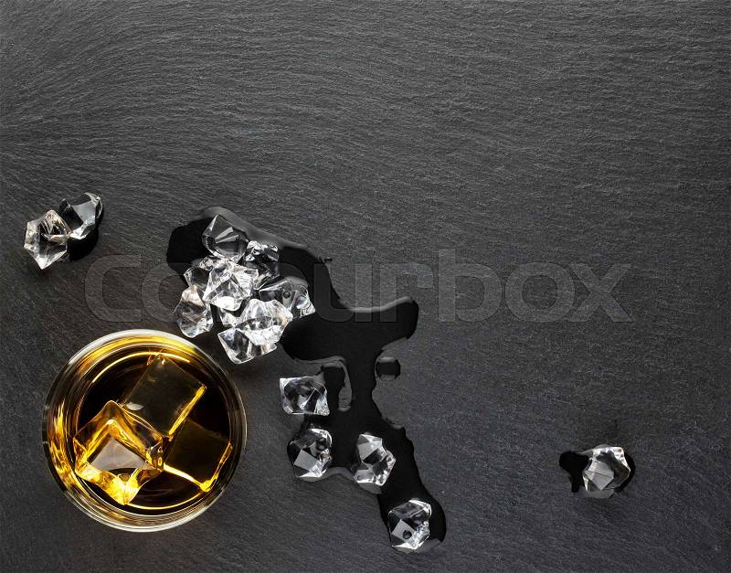 A glass of whiskey with ice and melted ice on slate blackboard, stock photo