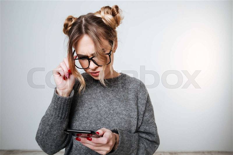 Surprised Woman in sweater and eyeglasses looking at phone. Isolated gray background, stock photo