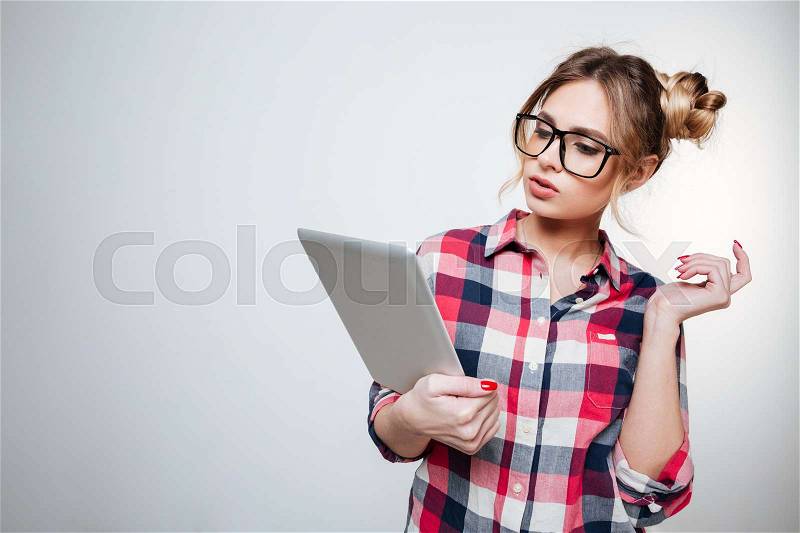 Woman in shirt and eyeglasses using tablet computer in studio. Isolated gray background, stock photo