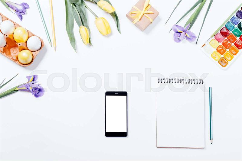 Easter composition: flowers, smart phone, painted eggs, watercolors and notebook. Top view, stock photo