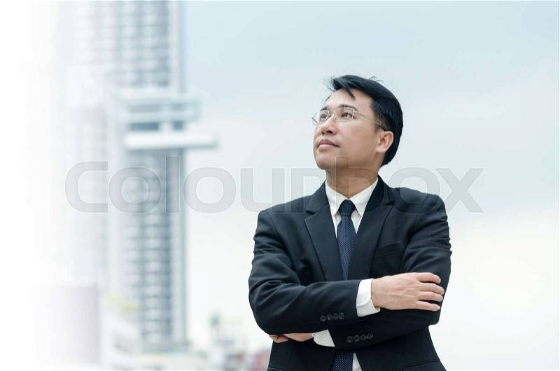 Portrait of asian businessman with arms crossed standing with city building background, stock photo