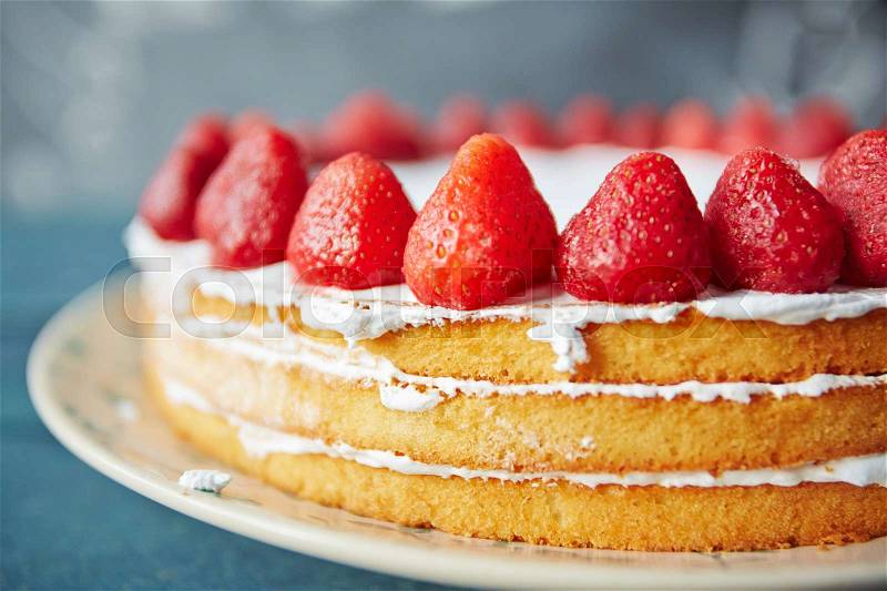 Closeup shot of simple creamy naked cake decorated with fresh ripe strawberries and white icing, stock photo
