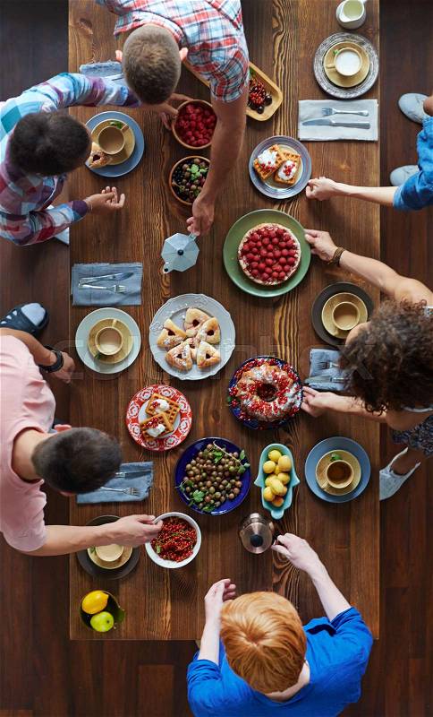 Directly above view of festive table covered with homemade pastry, fresh berries and fruits and people choosing meals beside, stock photo