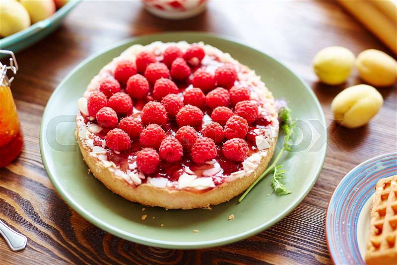 Close-up view of delicious freshly baked almond raspberry tart lying on green plate placed on wooden table, stock photo