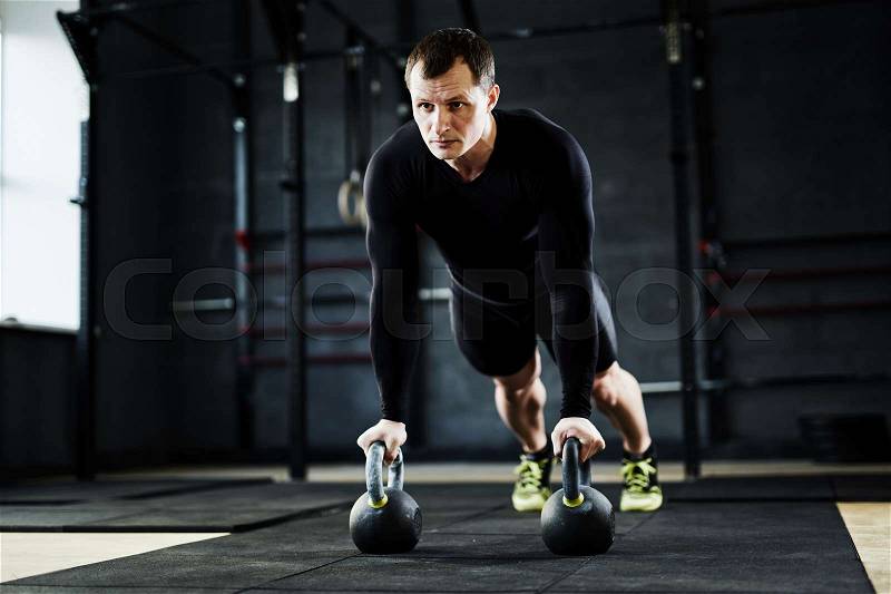Intense crossfit workout in gym: male athlete performing kettlebell pushups looking determined and strained, stock photo