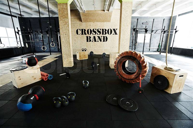 High angle shot of crossfit gym with modern equipment: wall mounted apparatus system, enormous tire, hammer, medballs, kettlebells, bar plates and jump boxes, stock photo