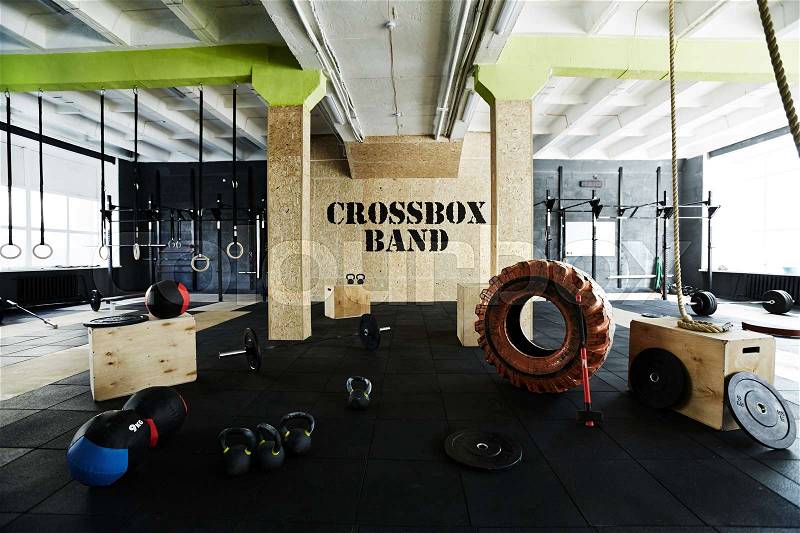 Wide angle shot of crossfit gym with modern equipment: wall mounted apparatus system, enormous tire, hammer, medballs, kettlebells, bar plates and jump boxes, stock photo