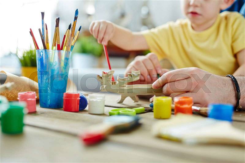 Pretty family of two attending art class and working on design of wooden toy with the help of brushes and gouache, close-up shot, stock photo