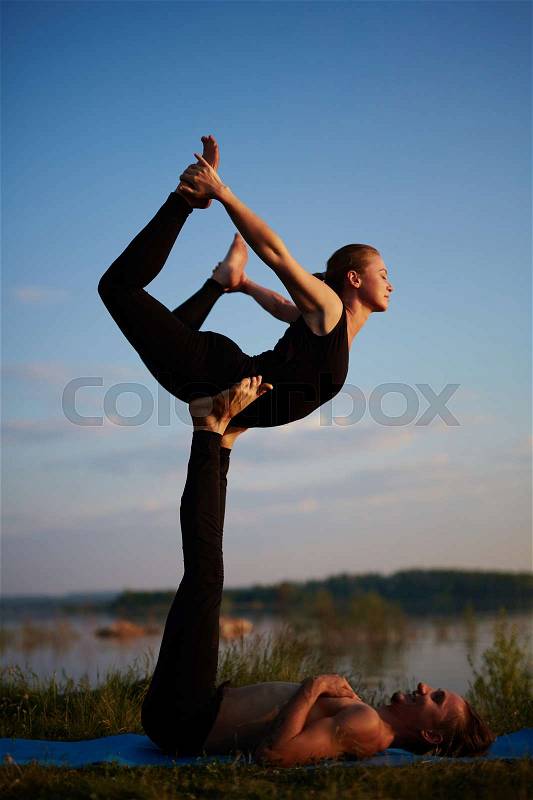 Experienced instructors balancing in front bird pose while doing acroyoga on late summer evening, stock photo