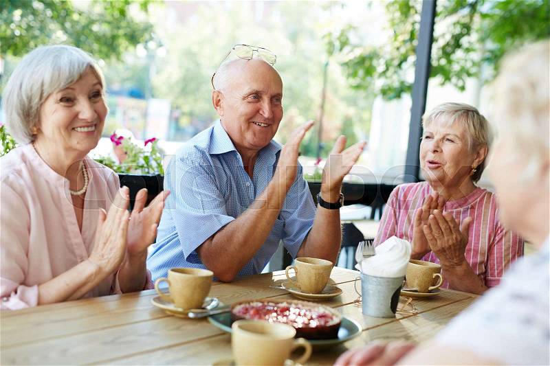 Group of smiling elderly people gathered together in outdoor cafe for tea-drinking and applauding joyfully, stock photo