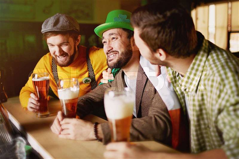 Old school mens get together in sports bar, patting each other on shoulders and drinking craft beer from tall glasses at counter, stock photo