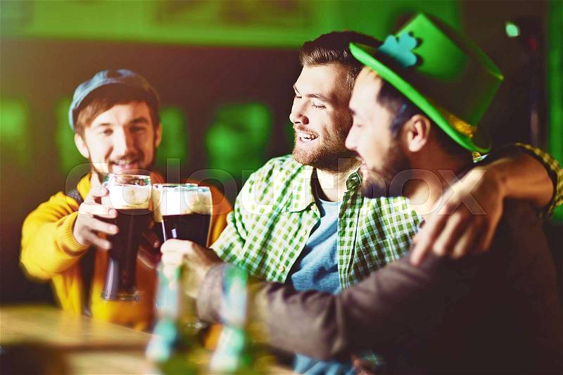 Saint Patricks day celebration in Irish pub: group of friends dressed in traditional green drinking dark beer from tall gasses at counter, stock photo