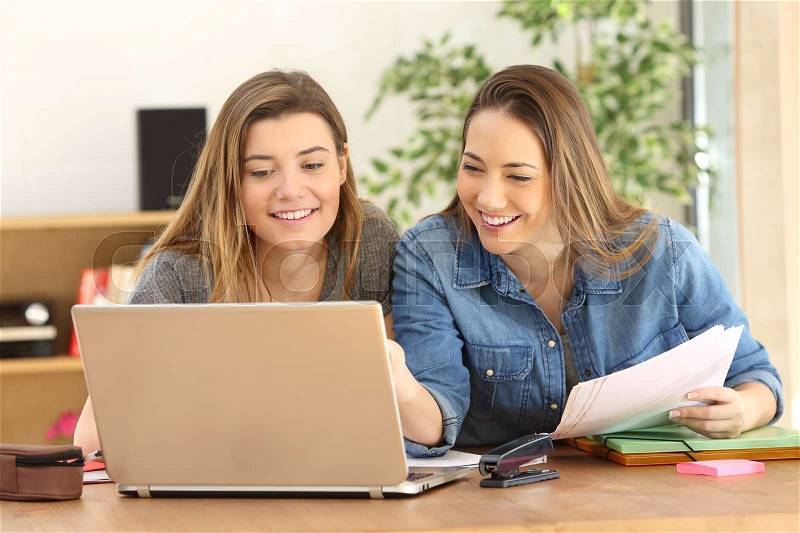 Two students studying together on line with a laptop in the living room at home with a homey background, stock photo