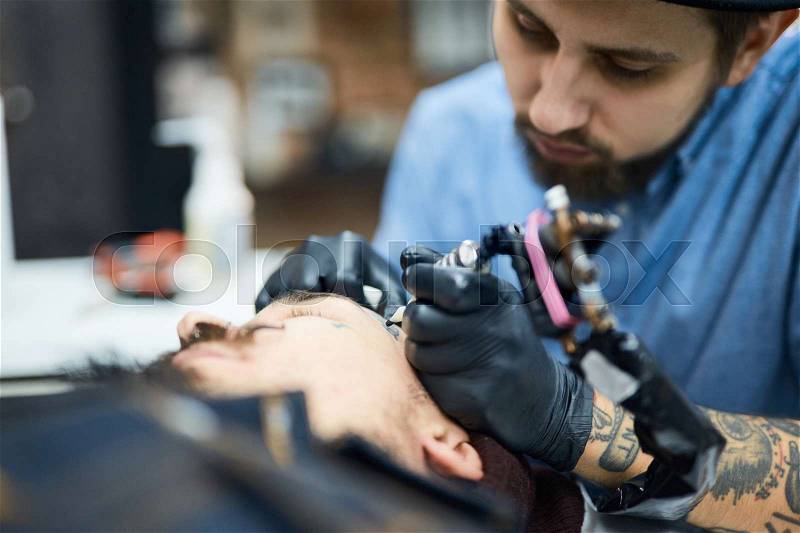 Tattooer drawing on face of his client, stock photo