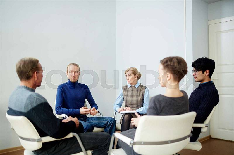 Several men and women sharing their troubles and discussing them at psychological session, stock photo